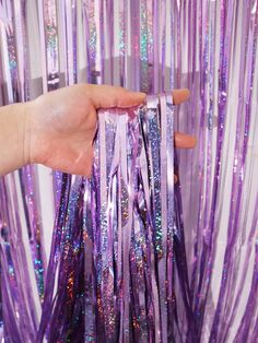 someone is holding some purple streamers in front of the curtain that has sequins on it