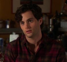 a man with curly hair wearing a red and black flannel shirt looking at the camera