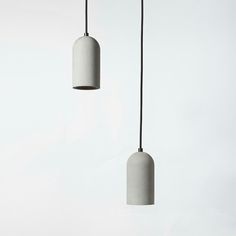 two concrete lamps hanging from black cords against a white wall with no one in it