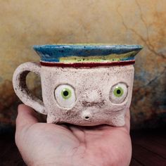 a hand holding a ceramic cup with eyes on it