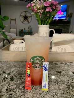 a starbucks drink next to a carton of candy on a counter in front of a vase with flowers