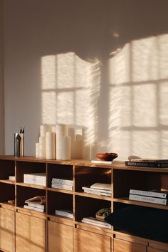 a book shelf with books and other items on it in front of a window that is casting long shadows