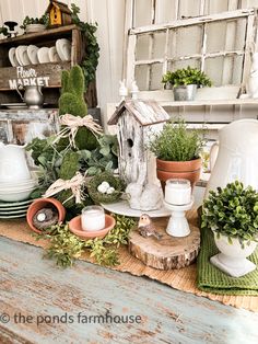 a table topped with potted plants next to a birdhouse on top of a piece of wood