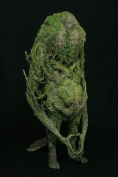 an artistic sculpture made out of moss and leaves on a black background, with the image of a man's face covered in vines