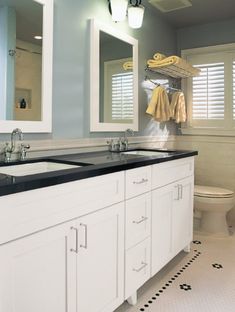 a white bathroom with black counter tops and two mirrors on the wall above the sinks