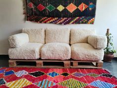 a white couch sitting on top of a red rug next to a wooden pallet