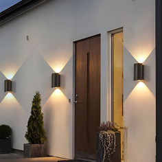 two lights on the side of a building with potted plants in front of it