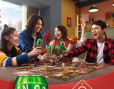 group of people sitting around a table holding up beer cans and playing games with each other