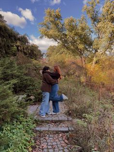 two people standing on a stone path in the woods with trees and bushes behind them