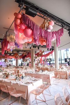 a room filled with lots of tables covered in pink and red balloons hanging from the ceiling