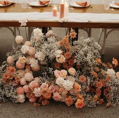 an arrangement of flowers on a table in front of candles and plates with napkins