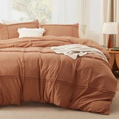 a bed with an orange comforter and pillows on top of it in front of a window