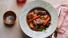 a bowl filled with meat and vegetables on top of a table next to a glass of wine