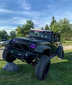 a black jeep parked on top of a grass covered field next to a rock and trees