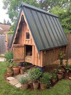 a small wooden house with a metal roof in the grass next to potted plants