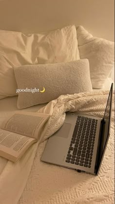 a laptop computer sitting on top of a bed next to an open book and pillow