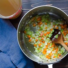 vegetables being cooked in a pan with a wooden spoon and blue napkin next to it