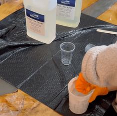 someone is pouring something out of a plastic cup on top of a table with other items