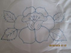 a close up of a flower on a white table cloth with blue stitching and leaves