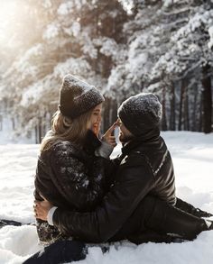 a man and woman sitting in the snow talking on their cell phones while holding each other