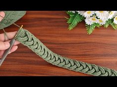 someone is crocheting the edge of a piece of green yarn with scissors on a wooden table