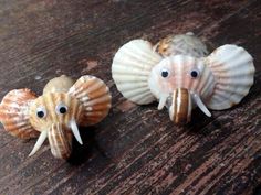 three seashells with googly eyes are sitting on a wooden table, one is in the shape of an elephant