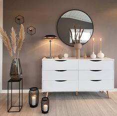 a white dresser sitting next to a mirror on top of a wooden floor covered in candles