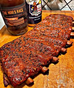 a large piece of meat sitting on top of a wooden cutting board next to a bottle of booze