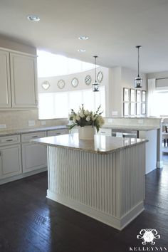 a large kitchen with an island in the center and white cabinets on both sides, along with two vases filled with flowers