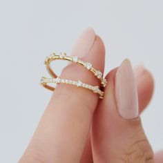 a woman's hand holding a gold ring with white stones on top and bottom