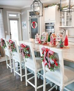 a kitchen decorated for christmas with wreaths and decorations on the counter top, along with white chairs