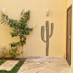 a large cactus is on the side of a building next to a small tree and door