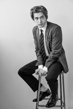 a man in a suit and tie sitting on a stool