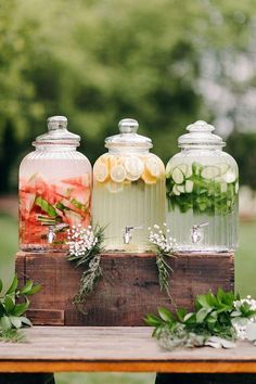 three jars filled with flowers and greenery on top of a wooden table in front of trees