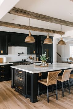 a large kitchen with black cabinets and white counter tops, gold pendant lights hanging from the ceiling