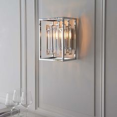 a wall light that is mounted to the side of a white wall next to some wine glasses