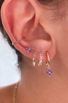 A woman wearing multiple gold earrings with purple stones. Cubic Zirconia Gemstone Huggie Earrings, Cubic Zirconia Gemstone Huggie Jewelry, Dainty Purple 14k Gold Jewelry, Dainty 14k Gold Purple Jewelry, Purple Gold Plated Jewelry For Gifts, Gold Plated Purple Jewelry For Gifts, Purple Gold Plated Jewelry Gift, Purple Gold-plated Jewelry Gift, Fine Jewelry Lavender Cubic Zirconia