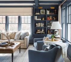 a living room filled with lots of furniture next to large windows and bookshelves