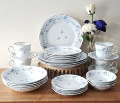 a table topped with lots of white and blue dishes next to a vase filled with flowers