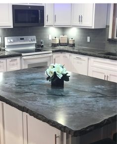 a kitchen with white cabinets and granite counter tops, along with a center island in the middle