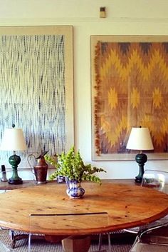 a dining room table with two lamps on each side and paintings above it in the background