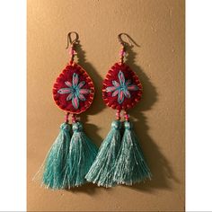 two pairs of earrings with tassels hanging from the hooks on a beige wall