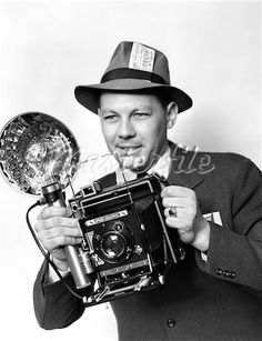 a man in a suit and hat holding an old camera