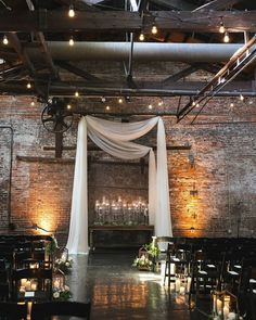 an indoor wedding venue with white draping and candles on the aisle, surrounded by brick walls