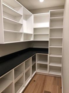 an empty walk in closet with white shelving and black countertop top on wooden flooring