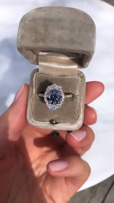 a woman's hand holding an engagement ring with a blue diamond in the center