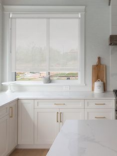 a kitchen with white cabinets and marble counter tops in front of a large open window