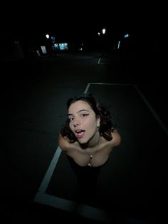 a woman is sitting in the middle of an empty parking lot at night with her mouth open