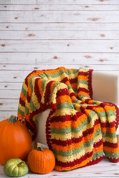 a crocheted blanket sitting on top of a white chair next to pumpkins