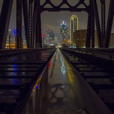 the city skyline is lit up at night as seen from an old train trestle